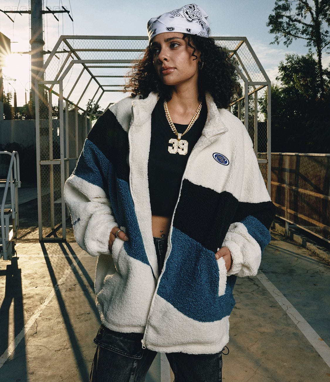 Aelfric Eden fleece layers styled beside an outdoor sports court